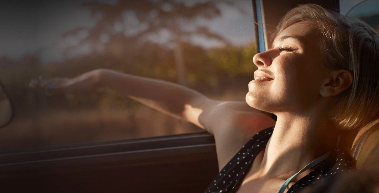 Person genießt Sonnenlicht durch Autofenster, entspannt mit geschlossenen Augen während einer Fahrt im Nissan.